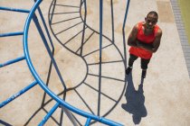 Портрет инвалида смешанной расы с протезным бегущим лезвием на открытом спортзале у побережья в беспроводных наушниках. Здоровый образ жизни. — стоковое фото