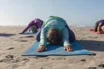 Groupe d'amies caucasiennes qui aiment faire de l'exercice sur une plage par une journée ensoleillée, pratiquer le yoga et s'asseoir en position de yoga. — Photo de stock