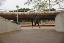 Ajuste mujer de raza mixta con hijab y ropa deportiva ejerciendo al aire libre en la ciudad, corriendo en un parque urbano. Ejercicio urbano. - foto de stock