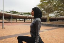 Впишеться змішана жінка в хіджаб і спортивний одяг, займається спортом на відкритому повітрі в місті, розігріваючись, розтягуючись в міському парку. Міський спосіб життя вправи . — стокове фото
