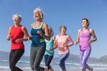 Grupo de amigas caucasianas que gostam de se exercitar em uma praia em um dia ensolarado, correndo na praia e sorrindo. — Fotografia de Stock