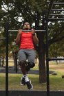 Hombre de raza mixta discapacitado con una pierna protésica, haciendo ejercicio en un parque en el gimnasio al aire libre, con auriculares inalámbricos en hacer pull-ups. Fitness discapacidad estilo de vida saludable. - foto de stock