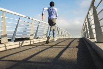 Vista trasera de la mujer de raza mixta en forma que usa hijab y ropa deportiva que hace ejercicio al aire libre en la ciudad en un día soleado, corriendo en una pasarela. Ejercicio urbano. - foto de stock