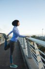 Fit gemischte Rennläuferin in Hijab und Sportbekleidung, die an einem sonnigen Tag im Freien in der Stadt trainiert und ihre Beine auf einer Fußgängerbrücke streckt. Bewegung im städtischen Lebensstil. — Stockfoto