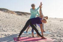 Grupo de amigas caucásicas disfrutando haciendo ejercicio en una playa en un día soleado, practicando yoga y de pie en posición de yoga. - foto de stock