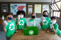Портрет групи з багатьох етнічних дітей, які носять маски для обличчя, що тримають пластикові предмети в класі в школі. Початкова освіта соціальне дистанціювання охорона здоров'я під час пандемії коронавірусу Covid19 . — стокове фото