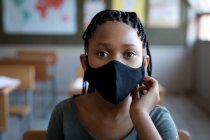 Portrait of a mixed race girl wearing a face mask, sitting on his desk in class at school. Primary education social distancing health safety during Covid19 Coronavirus pandemic. — Stock Photo