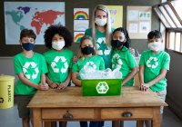 Retrato de una maestra caucásica y un grupo de niños multiétnicos que usan máscaras faciales con contenedor de reciclaje en la escuela. Educación primaria distanciamiento social de la seguridad sanitaria durante el Covid19 Coronavirus. - foto de stock