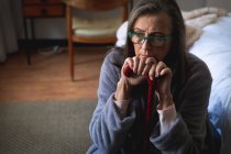 Стурбована кавказька жінка проводить час удома, спілкуючись на відстані та самотності в карантині, сидячи в спальні, тримаючи палицю.. — стокове фото