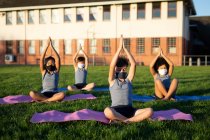 Gruppe multiethnischer Kinder mit Gesichtsmasken beim Yoga im Schulgarten. Grundschulbildung soziale Distanzierung der Gesundheitssicherheit während der Covid19 Coronavirus-Pandemie. — Stockfoto