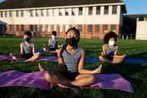 Група з багатьох етнічних дітей, які носять маски для обличчя, виконують йогу в шкільному саду. Початкова освіта соціальне дистанціювання охорона здоров'я під час пандемії коронавірусу Covid19 . — стокове фото