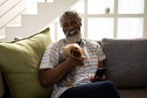 Uomo anziano afroamericano seduto su un divano, utilizzando uno smartphone, scattando un selfie, distanza sociale e isolamento in quarantena — Foto stock