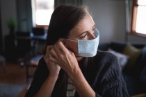 Caucasian woman enjoying time at home, social distancing and self isolation in quarantine lockdown, putting face mask on protecting from Covid 19 coronavirus infection. — Stock Photo