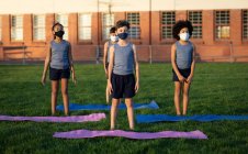 Grupo de crianças multi étnicas usando máscaras faciais realizando ioga no jardim da escola. Educação primária distanciamento social segurança sanitária durante Covid19 pandemia de coronavírus. — Fotografia de Stock