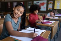 Eine Gruppe multiethnischer Kinder sitzt auf ihrem Schreibtisch im Klassenzimmer der Schule. Grundschulbildung soziale Distanzierung der Gesundheitssicherheit während der Covid19 Coronavirus-Pandemie. — Stockfoto