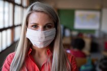 Portrait d'une enseignante caucasienne portant un masque facial en classe. Enseignement primaire distanciation sociale sécurité sanitaire pendant la pandémie de coronavirus Covid19. — Photo de stock