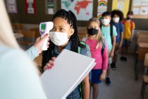 Insegnante donna caucasica che misura la temperatura dei bambini in una scuola elementare. Istruzione primaria distanza sociale sicurezza sanitaria durante la pandemia di Covid19 Coronavirus. — Foto stock