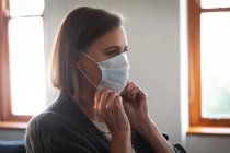 Caucasian woman enjoying time at home, social distancing and self isolation in quarantine lockdown, putting face mask on protecting from Covid 19 coronavirus infection. — Stock Photo