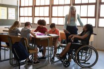 Disable mixed race girl sitting in her wheelchair and her female teacher using tablet in the classroom. Primary education social distancing health safety during Covid19 Coronavirus pandemic. — Stock Photo