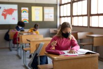 Multi ethnic group of elementary school children sitting at desks wearing face masks in classroom. Primary education social distancing health safety during Covid19 Coronavirus pandemic. — Stock Photo