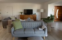 Современная, пустая гостиная с двумя серыми и одним зеленым диванами, большим экраном телевизора и ежедневными гаджетами, лежащими в современном доме — стоковое фото