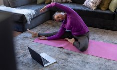 Kaukasische Frau genießt Zeit zu Hause, soziale Distanzierung und Selbstisolierung in Quarantäne, sitzt im Wohnzimmer mit Laptop auf dem Boden, trainiert, dehnt sich. — Stockfoto