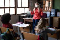 Kaukasische Lehrerin mit Gesichtsmaske, die in der Schulklasse unterrichtet. Grundschulbildung soziale Distanzierung der Gesundheitssicherheit während der Covid19 Coronavirus-Pandemie. — Stockfoto