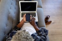 Старший афроамериканец, лежащий на диване, с ноутбуком, разговаривающий по телефону, социальное дистанцирование и самоизоляция в карантине — стоковое фото