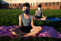 Due ragazzi multietnici che indossano maschere facciali che praticano yoga nel giardino della scuola. Istruzione primaria distanza sociale sicurezza sanitaria durante la pandemia di Covid19 Coronavirus. — Foto stock