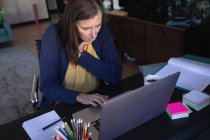 Femme caucasienne profitant du temps à la maison, de la distance sociale et de l'isolement personnel en quarantaine, assise à table, utilisant un ordinateur portable. — Photo de stock