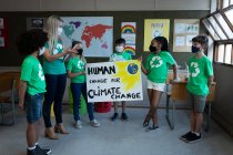 Maestra caucásica y grupo de niños multiétnicos que usan máscaras faciales y sostienen pancartas sobre el cambio climático en la escuela. Educación primaria distanciamiento social de la seguridad sanitaria durante el Covid19 Coronavirus. - foto de stock