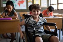 Portrait of disable Caucasian boy sitting in his wheelchair in the classroom during the lesson.  Primary education social distancing health safety during Covid19 Coronavirus pandemic. — Stock Photo