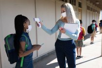 Insegnante donna caucasica con maschera facciale che misura la temperatura di una ragazza in una scuola elementare. Istruzione primaria distanza sociale sicurezza sanitaria durante la pandemia di Covid19 Coronavirus. — Foto stock
