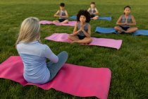 Group of multi ethnic kids and their female teacher wearing face masks performing yoga in the school garden. Primary education social distancing health safety during Covid19 Coronavirus pandemic. — Stock Photo