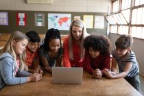 Female Caucasian teacher and multi ethnic group of kids using laptop during the lesson. Primary education social distancing health safety during Covid19 Coronavirus pandemic. — Stock Photo