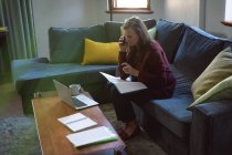 Kaukasische Frau genießt Zeit zu Hause, soziale Distanzierung und Selbstisolierung in Quarantäne, sitzt auf dem Sofa im Wohnzimmer, benutzt einen Laptop, telefoniert. — Stockfoto