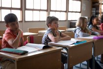 Groupe d'enfants multiethniques assis sur leur bureau dans la salle de classe à l'école. Enseignement primaire distanciation sociale sécurité sanitaire pendant la pandémie de coronavirus Covid19. — Photo de stock