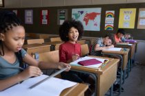 Un gruppo di ragazzi multietnici seduti sulla scrivania in classe a scuola. Istruzione primaria distanza sociale sicurezza sanitaria durante la pandemia di Covid19 Coronavirus. — Foto stock
