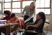 Behinderte Mischlingshündin im Rollstuhl und ihre Lehrerin mit Tablet im Klassenzimmer. Grundschulbildung soziale Distanzierung der Gesundheitssicherheit während der Covid19 Coronavirus-Pandemie. — Stockfoto