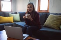 Kaukasische Frau genießt Zeit zu Hause, soziale Distanzierung und Selbstisolierung in Quarantäne, sitzt auf dem Sofa im Wohnzimmer, benutzt einen Laptop, hat Videoanrufe. — Stockfoto