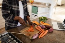 Homem de pé em uma cozinha, cortando legumes com uma faca, distanciamento social e auto-isolamento em bloqueio de quarentena — Fotografia de Stock