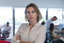 Portrait of confident Caucasian female business creative with arms crossed looking to camera, colleagues working in the background. Creative business professionals working in a busy modern office. — Stock Photo