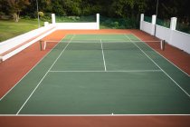 Una vista di un campo da tennis vuoto con una rete al centro in una giornata di sole, foresta sullo sfondo — Foto stock
