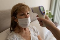 Mulher branca sênior em casa visitada por enfermeira caucasiana, verificando a temperatura. Cuidados médicos em casa durante a quarentena do Coronavirus Covid 19. — Fotografia de Stock