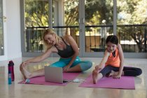 Caucasian woman and her daughter spending time at home together, doing yoga, stretching, using laptop computer. Social distancing during Covid 19 Coronavirus quarantine lockdown. — Stock Photo