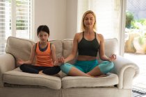 Caucasian woman and her daughter spending time at home together, doing yoga, meditating. Social distancing during Covid 19 Coronavirus quarantine lockdown. — Stock Photo