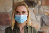 Portrait of Caucasian woman spending time at home, wearing face mask and looking at camera. Social distancing during Covid 19 Coronavirus quarantine lockdown. — Stock Photo