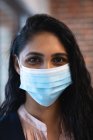 Portrait of mixed race woman working in a casual office, wearing face mask and looking at camera. Social distancing in the workplace during Coronavirus Covid 19 pandemic. — Stock Photo