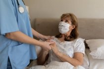 Mulher caucasiana sênior em casa visitada por enfermeira caucasiana, de pé e de mãos dadas. Cuidados médicos em casa durante a quarentena do Coronavirus Covid 19. — Fotografia de Stock