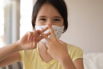 Retrato de menina caucasiana passar o tempo em casa, usando máscara facial, olhando para a câmera, usando linguagem gestual. Distanciamento social durante o bloqueio de quarentena do Covid 19 Coronavirus. — Fotografia de Stock